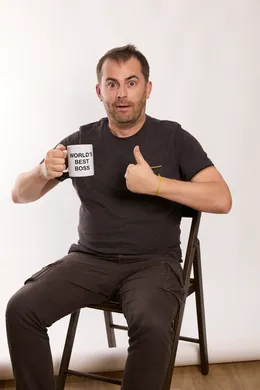homme assis sur une chaise qui tient un mug dans un main et fait un pouce avec l'autre main
